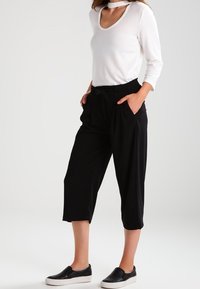 Haut blanc à manches longues avec un col en U et un détail de collier ras du cou, associé à un pantalon noir ample et court avec des poches et une taille cintrée.