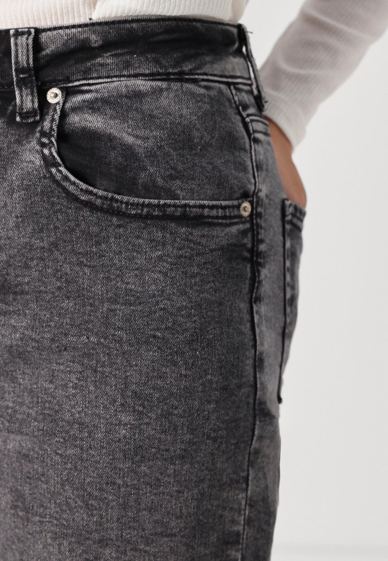 Schwarze Jeans aus Denim mit schlanker Passform, ausgestattet mit einer Vordertasche, silbernen Beschlägen und einer weichen Textur. Der Stoff wirkt leicht ausgebleicht.