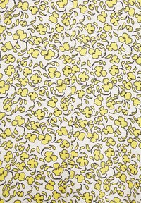 Motif floral jaune avec contours noirs sur tissu blanc, montrant une couture centrée courant verticalement à travers le design.