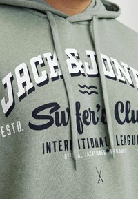 Sudadera verde de mezcla de algodón con texto en blanco y azul marino, capucha con cordón y gráficos con temática de surf.