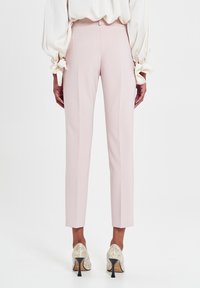 Helle rosa maßgeschneiderte Hose mit slim fit und gebügelten Falten, kombiniert mit glänzenden silbernen High-Heels. Weicher Stofftexture.