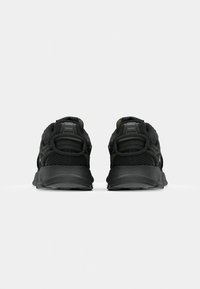 Chaussures de sport noires avec une tige en mesh, un design structuré, un talon rembourré et une semelle en caoutchouc ; elles comportent des lacets bouclés proéminents et des accents texturés.