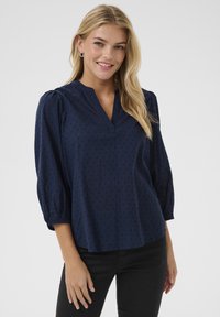 Blusa blu navy con scollo a V, maniche a tre quarti a sbuffo, motivo testurizzato e vestibilità comoda. Realizzata in tessuto leggero per garantire il massimo comfort.