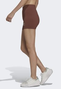 Osoba jde ve hnědých šortkách s vysokým pasem a malým logem na levém stehně, a v bílých sportovních teniskách s tlustými podrážkami.