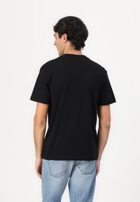 Sort bomulds t-shirt med korte ærmer, rund halsudskæring og et enkelt design. Kombineret med lyseblå jeans, der viser en afslappet pasform.