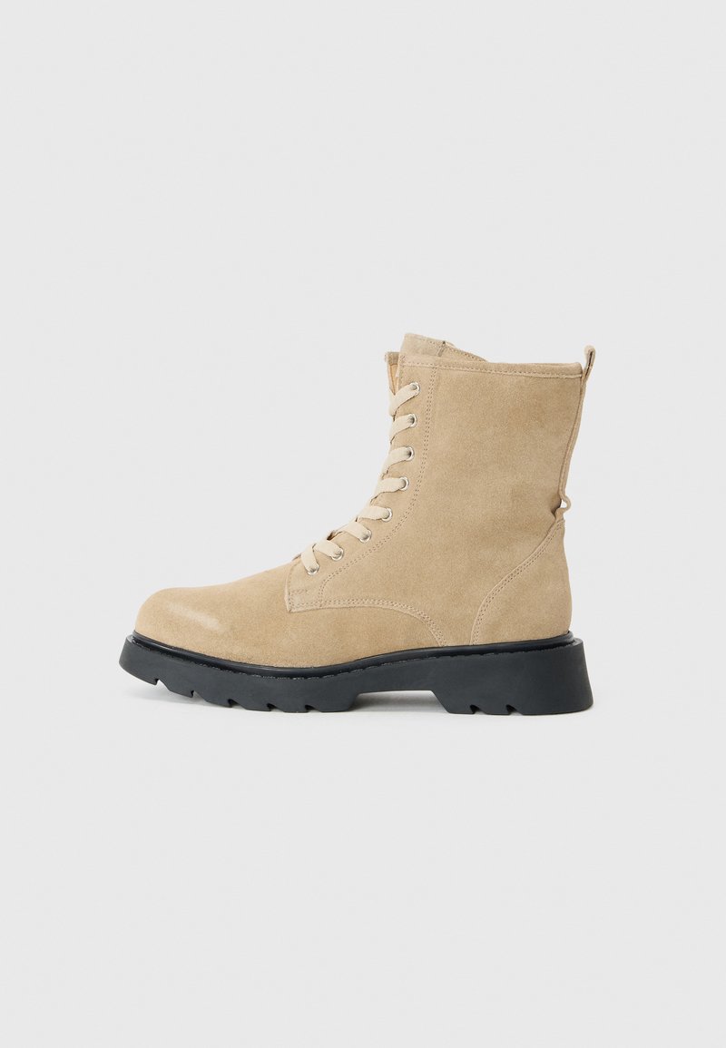 Botas de tobillo de ante beige con puntera redonda, diseño con cordones, cuello acolchado y suela de goma texturizada negra.