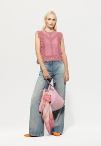 Rosa Spitzen-Top ohne Ärmel mit gewellten Kanten, getragen mit hellblauen weit geschnittenen Jeans. Helle rosa Tasche mit einem gemusterten Schal, orangefarbene spitze Schuhe.