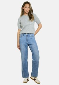 Pull gris à manches courtes associé à un jean taille haute à jambes larges bleu clair et des baskets crème avec des accents marron. Design simple et décontracté.