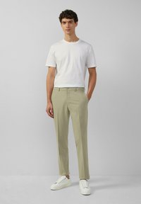 Hellgrüne Hose mit schmaler Passform und glatter Textur, kombiniert mit einem schlichten weißen T-Shirt und weißen Sneakers. Minimalistisches Design.