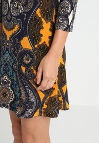 Robe multicolore présentant un motif cachemire complexe en bleu marine, orange et sarcelle. Elle possède des manches trois-quarts et un ourlet évasé.