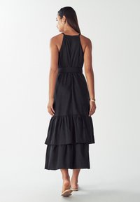 Čierna maxi šaty s vodorovnými ramienkami, vyrobené z ľahkej textílie. Majú priliehajúci pás a niekoľko volánových vrstiev na leme.