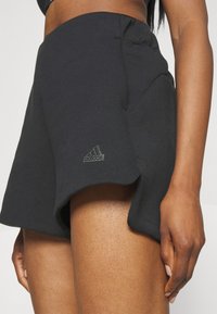 Shorts de sport noirs en tissu doux, avec un design en A, des détails de superposition et un logo adidas subtile en gris.