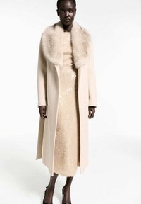 Beige wool coat with a faux fur collar, layered over a sparkly gold dress. The coat features long sleeves and a straight-cut silhouette.