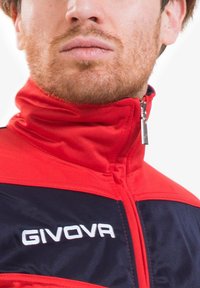 Giacca zip-up rossa e blu con colletto alto, con il nome del brand "GIVOVA" ricamato in bianco sul petto. Texture del tessuto liscia.