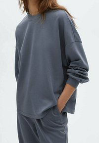 Gray cotton sweatshirt with a relaxed fit, round neck, and dropped shoulders. The fabric appears smooth with a soft texture.