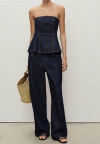 Top peplum sin mangas de denim oscuro combinado con pantalones anchos de denim oscuro. Un bolso de mimbre y sandalias negras completan el look.