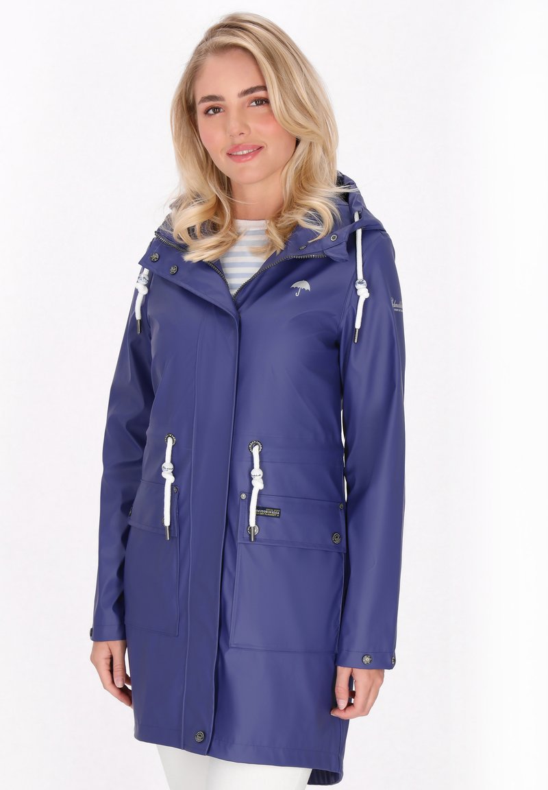 Lila vattentät regnjacka med huva, justerbara dragsnören, två framlådor och silverfärgade detaljer. Slät yta och medellång design.