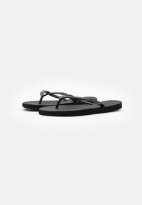 Des tongs noires en caoutchouc avec des fines lanières et un semelle texturée. Comprend un petit accent métallique sur la lanière. Design plat et décontracté.