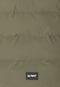 Olivengrøn puffjakke med quilted design, syede linjer og et sort mærke med teksten "SLOPE®" i nederste højre hjørne.