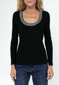 Haut noir à manches longues avec texture côtelée, doté d'un large décolleté en scoop orné de clous en argent décoratifs. Assorti avec un jean bleu.
