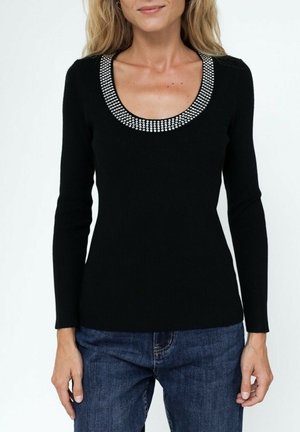 Haut noir à manches longues avec texture côtelée, doté d'un large décolleté en scoop orné de clous en argent décoratifs. Assorti avec un jean bleu.