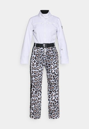 Jachetă albă de schi cu guler înalt, buzunare cu fermoar, asociată cu pantaloni de schi cu imprimeu leopard, având o talie neagră și dungi laterale.