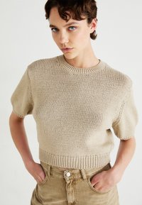 Μπεζ πλεκτό πουλόβερ κοντομάνικο με ριμπ τελείωμα στον λαιμό και το στρίφωμα. Μαλακή υφή και άνετη εφαρμογή, συνδυασμένο με καφέ παντελόνι κόρντουρα ψηλόμεσο.