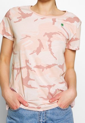 Lyserød t-shirt med et camouflage-mønster i mørkere lyserøde nuancer. Rund halsudskæring, korte ærmer og et lille grønt logo på brystet.