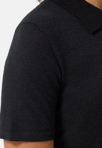 Kortsleeved svart stickad polo skjorta med klassisk krage och mjuk textur, med en figurnära design och minimala sömnadsdetaljer.