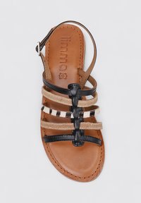 Sandal de cuero marrón con correas negras, beiges y estampadas. Diseño de punta abierta, suela plana, correa de tobillo ajustable y detalle de plantilla con marca.