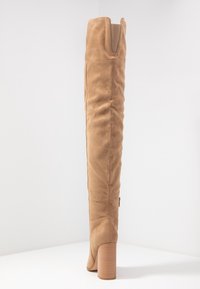 Stivale in suede tan fino al ginocchio, con punta arrotondata, asta texturizzata e un robusto tacco a blocco rigato. Include una zip laterale per facilitare l'accesso.