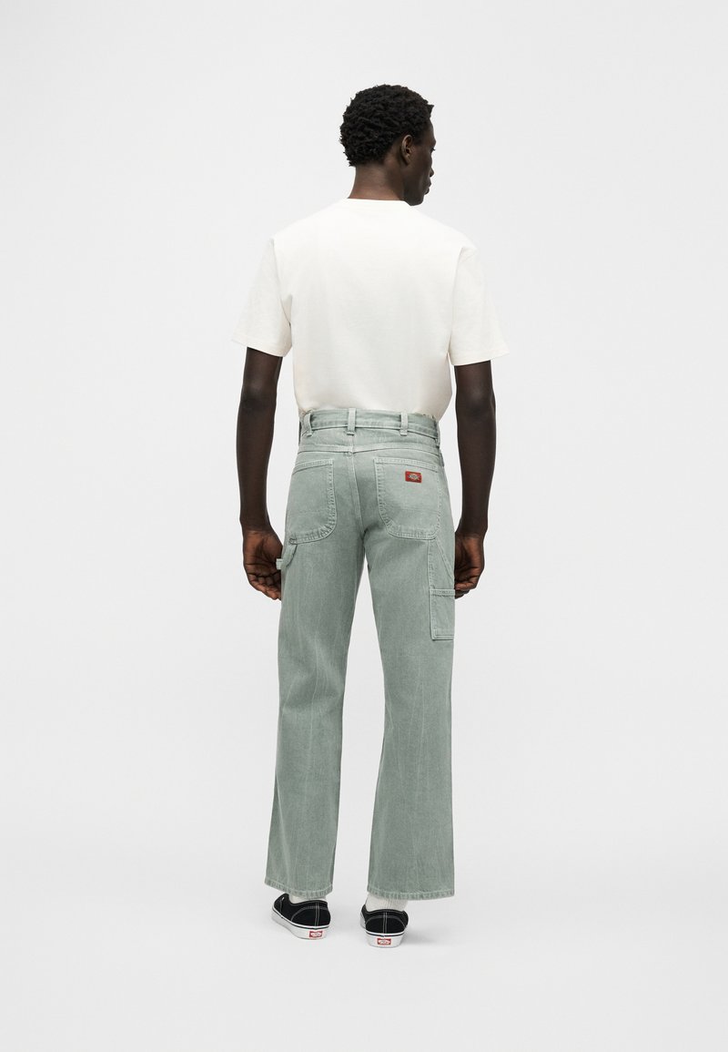 Lichtgroene wijde cargobroek met meerdere zakken, een hoge taille en een rood logopatch, gecombineerd met een eenvoudige witte T-shirt.