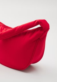 Borsa in tessuto rosso con una forma curvata, dotata di chiusura con zip e manico corto e arrotondato. Texture liscia con una leggera lucentezza.