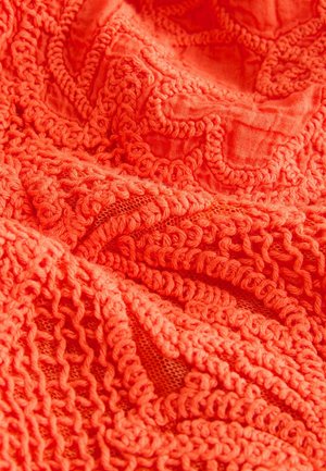 Heleoranž tekstiil tekstuursete mustritega. Omaduseks keerukad silmused ja punumised, mis näitavad nii massiivseid kui ka avatud võrgu alasid.