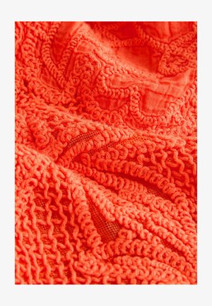 Heleoranž tekstiil tekstuursete mustritega. Omaduseks keerukad silmused ja punumised, mis näitavad nii massiivseid kui ka avatud võrgu alasid.