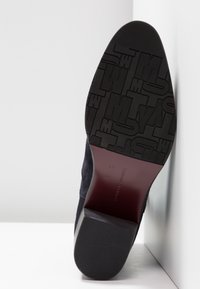 Námořnické semišové boty s texturovanou černou gumovou podrážkou, která má embossované logo, a elegantní hnědý akcent na patě.