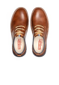 Zapatos de cuero marrón con forma redondeada, costuras en contraste y cordones ligeros. Cuentan con una plantilla acolchada y suela de goma con acentos sutiles.