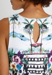 Mouwloze jurk met kleurrijk palm- en bloemenpatroon, textuur wit stof, sleutelgatdetail op de rug en kleine knoopsluiting.