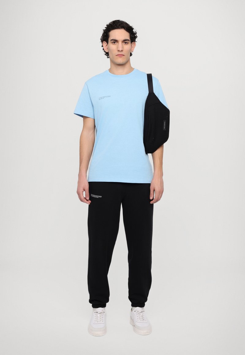 Light blue cotton t-shirt, black sweatpants, and a black shoulder bag. White sneakers with a thick sole. Minimalistic design with text details.
