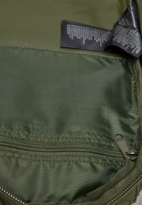 Olive green fabric bag interior with a zippered pocket, smooth texture, and a black care label with white text against the green background.