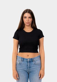 Černý, přiléhavý, krátký rukáv crop top vyrobený z žebrované látky, v kombinaci se světle modrými džíny s vysokým pasem, které odhalují břicho.