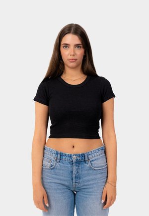 Juodas, prigludęs, trumpomis rankovėmis ap Crop top'as, pagamintas iš įpjautą audinį, derinamas su šviesiai mėlynomis aukšto liemens džinsomis, atskleidžiančiomis pilvą.