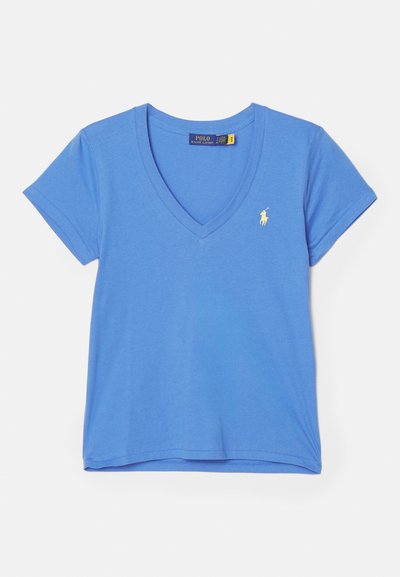 Zila kokvilnas T-kreklā ar V-veida kakla dizainu, īsām piedurknēm un mazu dzeltenu izšūtu logotipu kreisajā krūtī. Gluda tekstūra.