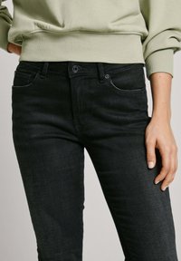 Juodi džinsai su liesu siluetu, su mygtuku ir užtrauktuku, penkiais kišenėmis ir subtiliomis siuvimo detalėmis siūlėse.