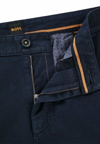 Navy blue trousers with a dark zipper and button closure. Features orange accents on the waistband and patterned inner lining.
