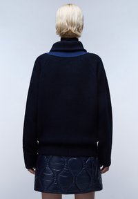 Granatowy sweter dzianinowy z wysokim kołnierzem, połączony z błyszcząca granatową mini spódnicą o pikowanym wzorze i widocznymi detalami szwów.