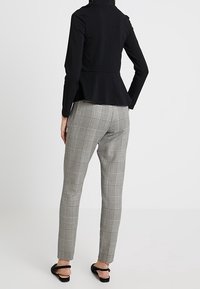 Schwarzes Peplum-Top kombiniert mit grauen karierten Hosen. Das Top hat einen hohen Ausschnitt und eine figurbetonte Passform; die Hosen haben eine schmale Passform mit einem karrierten Muster.