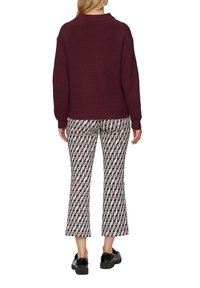 Bordeauxfarbener gerippter Strickpullover mit Rundhalsausschnitt, kombiniert mit gemusterten creme- und burgunderfarbenen Cropped-Hosen mit geometrischem Design.