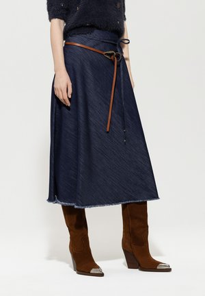 Denim skirt in dark blue with frayed hem, cinched at the waist with a brown leather belt. Paired with brown suede knee-high boots.