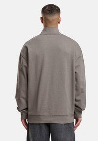 Sweatshirt gris surdimensionné avec un col haut, des poignets et un ourlet côtelés, et une finition en tissu lisse et texturé. Vue arrière présentée.